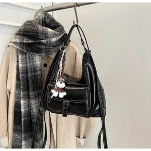 Detail of black glossy shoulder bag with buckle pocket and cute dog charm ornament