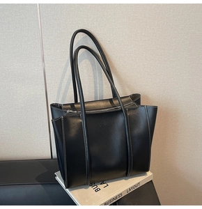 Detail of black leather tote bag featuring contrast stitching and embossed fashion text