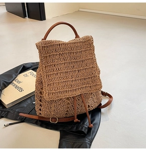 Detail of woven straw backpack with brown leather straps next to a fashion book