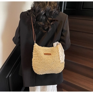 Detail of woven straw shoulder bag with lace bow and leather patch on model