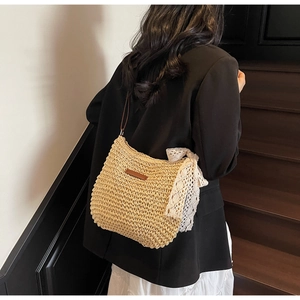 Detail shot of a beige straw bucket bag with delicate white lace bow and leather strap