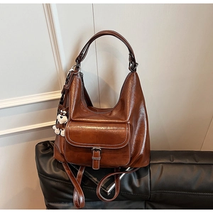 Detail view of a vintage brown oil-wax leather backpack with buckle pocket and white charm