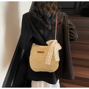 Close-up of woven straw tote bag with a large white lace bow and brown leather strap