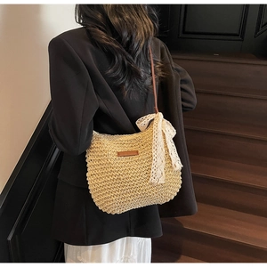 Detail of hand-woven straw crossbody bag with white lace bow and brown leather strap