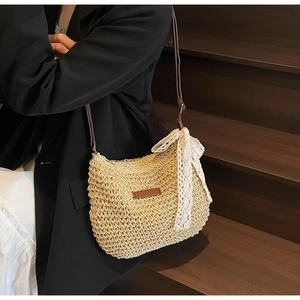 Detail of hand-woven straw bucket bag with white lace bow and brown leather strap