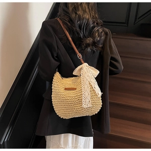 Detail of woven straw bucket bag featuring a white lace bow and adjustable leather strap