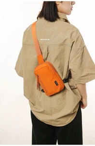 Detail of orange nylon crossbody bag with adjustable strap worn over a khaki shirt