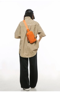 Detail of a bright orange nylon crossbody bag with adjustable strap and multiple zippers