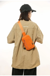 Detail view of vibrant orange nylon crossbody bag on a model showing a sporty casual look