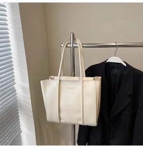 Detail view of cream leather tote bag with FASHION text hanging on a rack