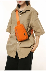 Detail of orange nylon crossbody bag featuring black buckle and zip pocket for outdoor use