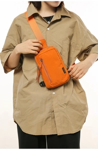 Detail of bright orange nylon crossbody bag with adjustable strap and front zipper