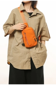 Detail of bright orange nylon crossbody bag with zipper pockets and wide strap