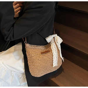 Detail shot of woven straw hobo bag featuring a white lace bow and dark brown strap