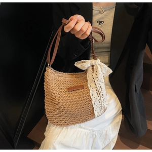Detail of hand-woven straw hobo bag with large white lace bow and brown leather strap