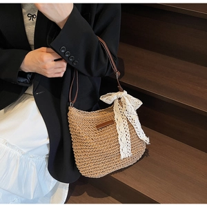 Detail of hand-woven straw tote with elegant white lace bow and brown leather shoulder strap