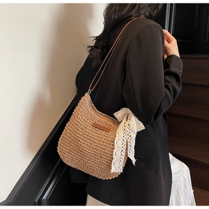 Detail of woven straw shoulder bag with white lace bow and brown leather strap on model