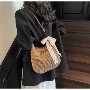 Detail of hand-woven straw crossbody bag with white lace bow and leather strap