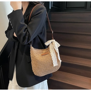 Close-up of woven straw shoulder bag featuring a large cream lace bow and leather strap