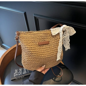 Detail of hand-woven straw crossbody bag featuring lace bow and leather strap detail