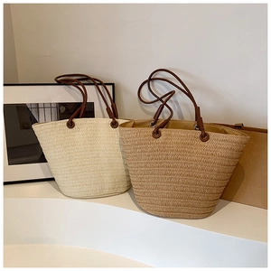 Detail of woven straw tote bags in beige and khaki with brown leather handles and metal rings