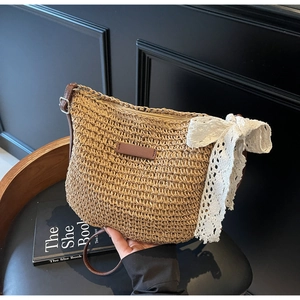 Detailed shot of straw shoulder bag with leather strap and white lace bow on black chair