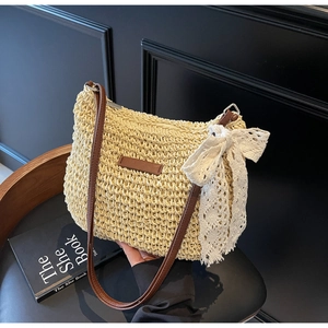 Detail of hand-woven straw crossbody bag with brown leather strap and white lace bow