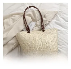 Detail of woven straw tote bag texture with slim brown handles on a white fabric surface