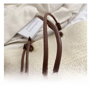 Close-up of woven straw tote bag featuring brown leather cylindrical handles and fine stitching