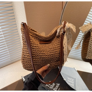 Close-up of hand-woven straw shoulder bag with leather strap and white lace bow detail