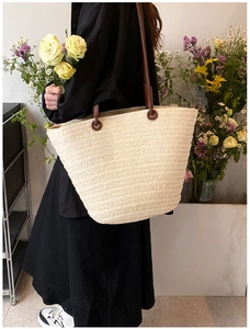 Detail of light beige straw tote bag with brown leather straps on woman shoulder