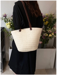 Detail of a large woven straw tote bag with brown faux leather straps for summer fashion