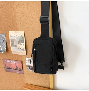 Detail of black nylon crossbody bag featuring front zipper pocket and woven brand label