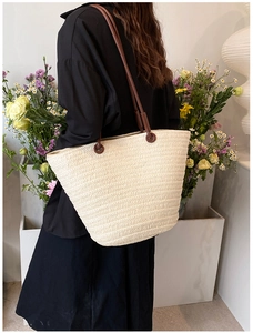 Detail of a beige woven straw tote bag with brown leather handles and metal ring accents
