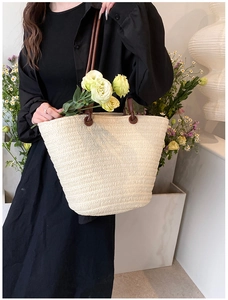 Model showing large beige straw woven bucket tote bag with dark brown leather handles