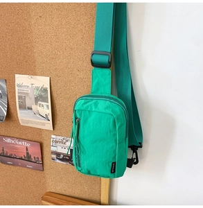 Detail of green nylon crossbody bag with adjustable strap and dual zipper pockets