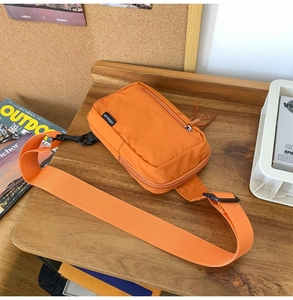 Detail of orange nylon crossbody bag featuring black zippers and side brand label on wood
