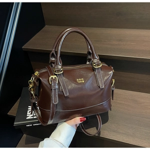 Detail of dark brown Boston bag with glossy finish and white contrast stitching