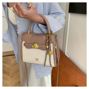 Detail of mocha and cream crossbody bag with a gold bear buckle and woven pendant