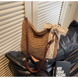 Detail of woven straw bucket bag featuring a large white lace bow and leather strap