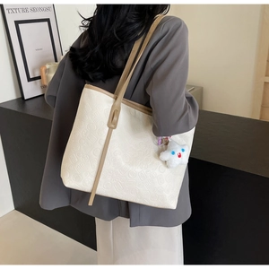 Close-up of cream tote bag featuring embossed mahjong patterns and a star plush charm