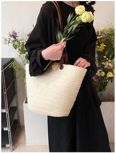 Close-up of woven straw tote bag with brown faux leather handles and floral background