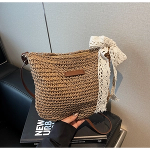 Detail of woven straw bucket bag featuring a white lace bow and brown leather strap