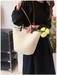 Detail of a woven beige tote bag featuring brown leather handles and textured straw pattern