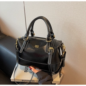 Detail of black glossy Boston bag with gold hardware and white contrast stitching