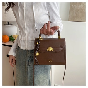 Macro detail of gold dog-shaped buckle and fringe charm on brown leather handbag