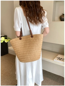Detail of hand-woven straw tote bag with brown shoulder straps in a minimalist setting