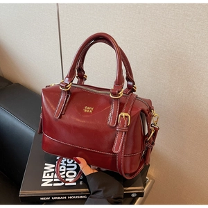Macro shot of a deep red Boston bag featuring contrast stitching and gold metal hardware