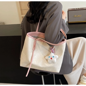 Detail of large tote bag with embossed textures and pink handles worn by a model
