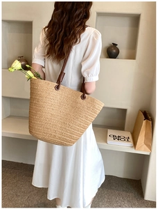 Close-up of woven straw tote bag featuring brown leather handles and circular hardware